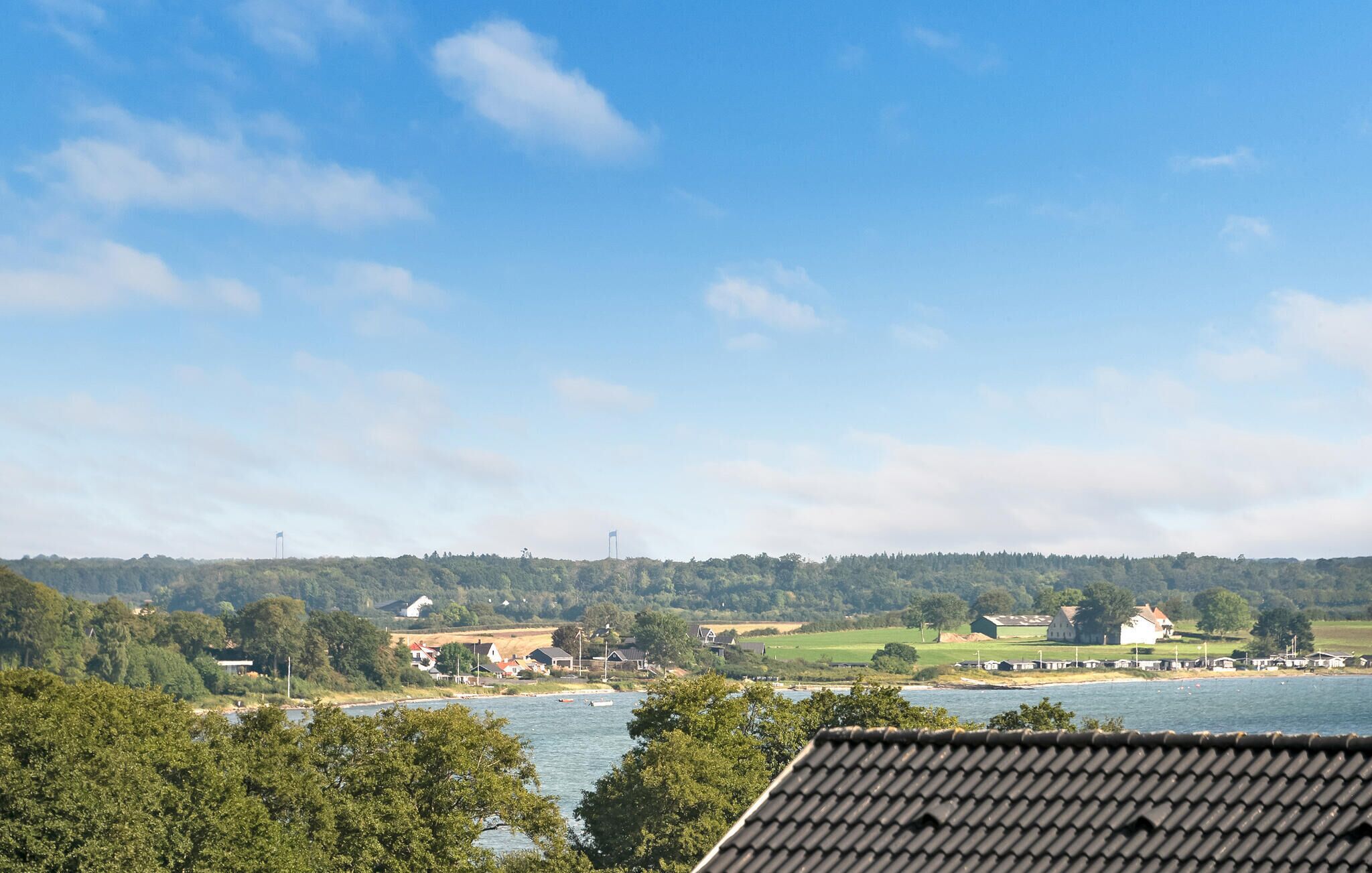 A coastal landscape with houses, a river, and a forested hill.