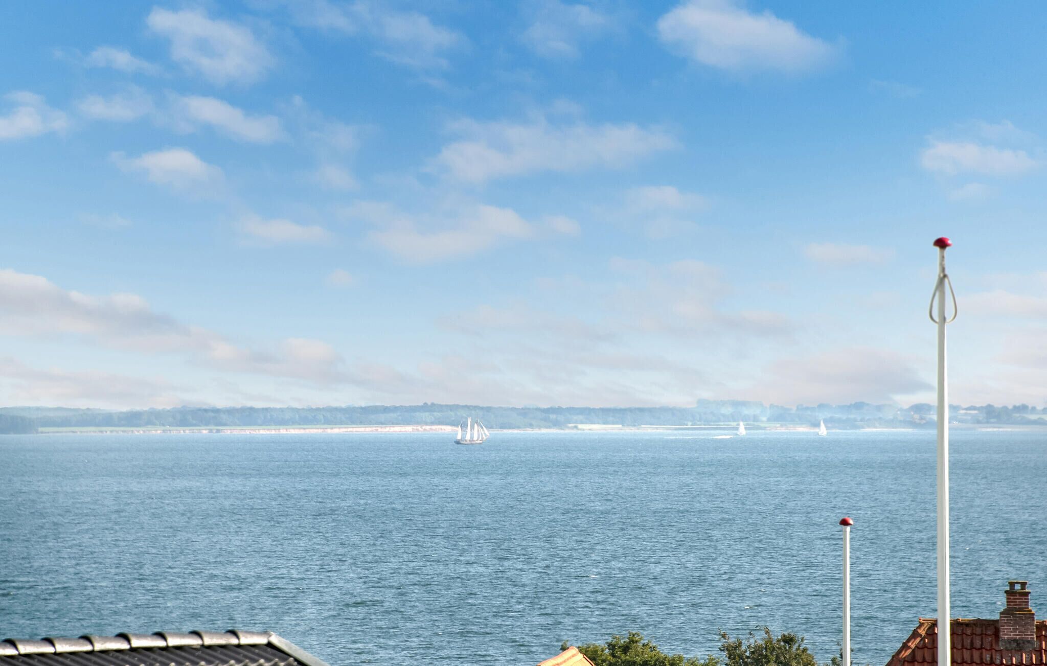A coastal view with a lighthouse, calm sea, and distant sailboats.