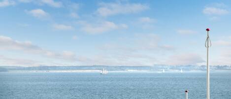 A coastal view with a lighthouse, calm sea, and distant sailboats.