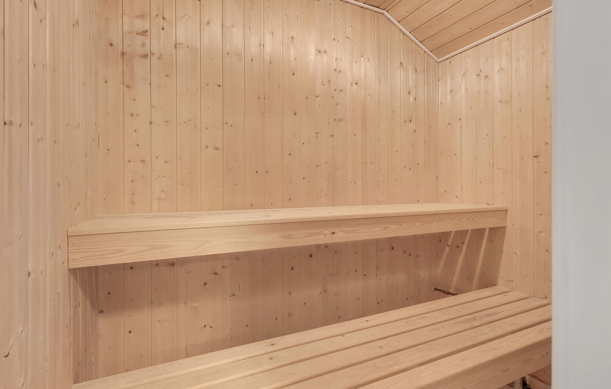 Puisesta laudelankusta rakennettu sauna, jossa on kaksi penkkiä ja kalteva katto.