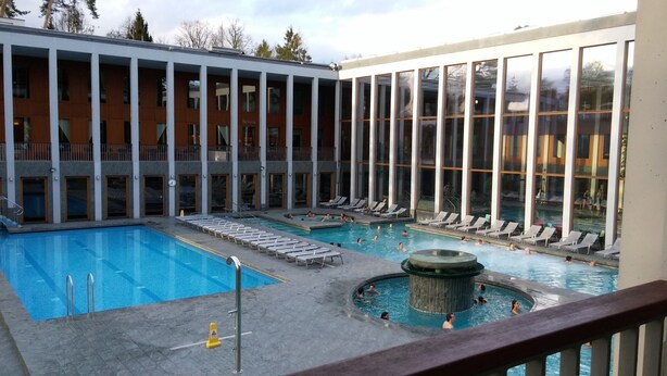 Ein Poolbereich mit Liegestühlen und einem Whirlpool, umgeben von einem Gebäude mit großen Fenstern und einem Balkon.