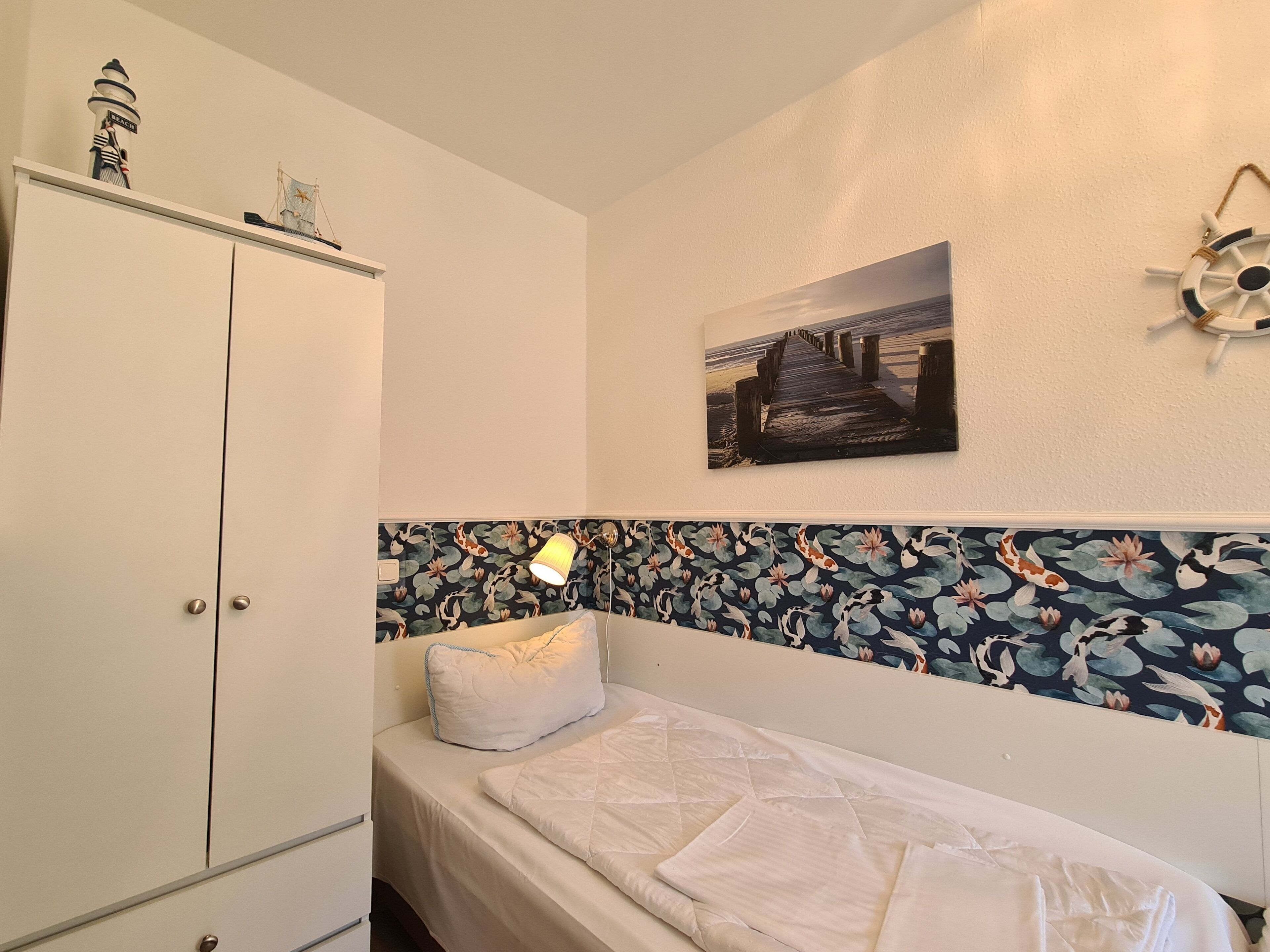 Une chambre à coucher comprenant un lit, une armoire, une lampe fixée au mur, un élément décoratif mural et une tête de lit à motifs floraux.