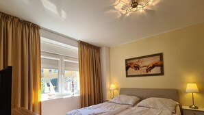 A hotel room with a bed, two bedside lamps, a painting on the wall, and a television on a wooden table.
