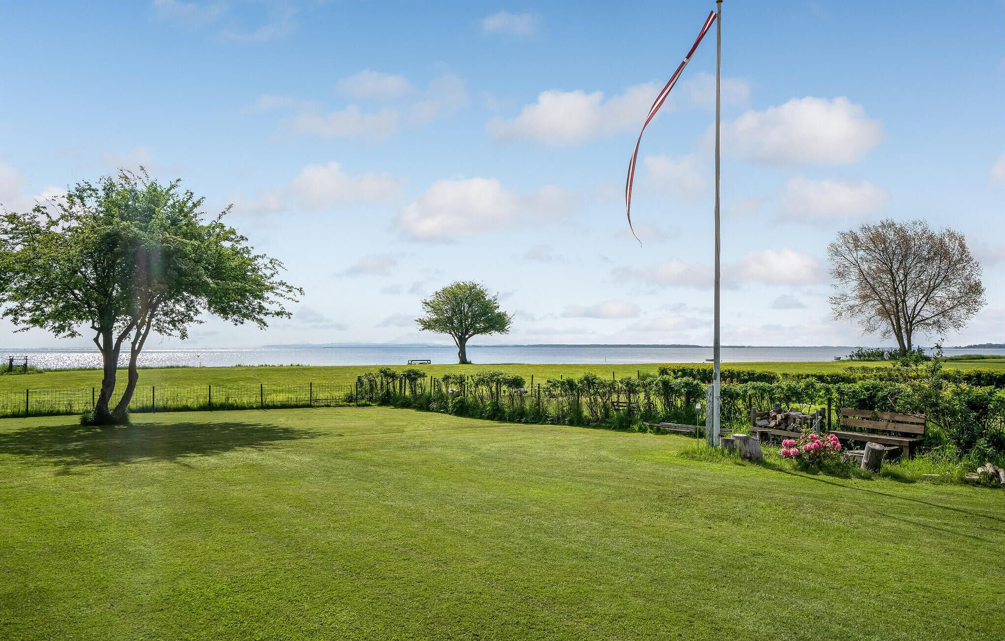 En græsmark med flagstang, træer og en bænk.