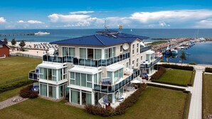 Un moderno hotel a più piani con ampie finestre, una zona esterna coperta e vista sul porto turistico e sul mare.