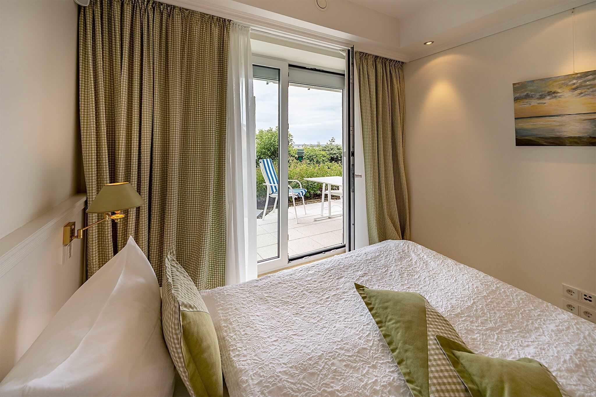Un dormitorio con cama, cortinas, una lámpara y un cuadro en la pared.