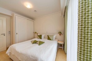 A bedroom with a large bed, bedside tables, a wardrobe, and a window with curtains.