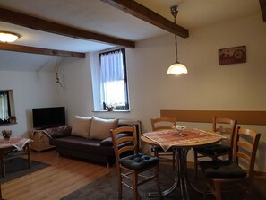Un salon confortable avec un canapé, une table à manger et des chaises, un téléviseur et une fenêtre avec des rideaux.