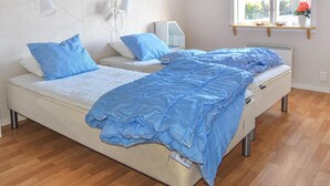 A double bed with a white mattress and blue bedding, a bedside table, a wall-mounted lamp, and a window with a view of the outdoors.