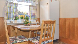 A compact kitchen with a wooden table, chairs, a refrigerator, and a window with curtains.