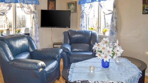 A living room with two leather armchairs, a flat-screen TV, and a coffee table with a vase of flowers.