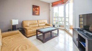 Una sala de estar moderna con un sofá color beige, una mesa de centro de vidrio, un televisor y un cuadro en la pared.