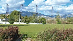 Un campo de golf con banderas, exuberante vegetación y montañas al fondo.
