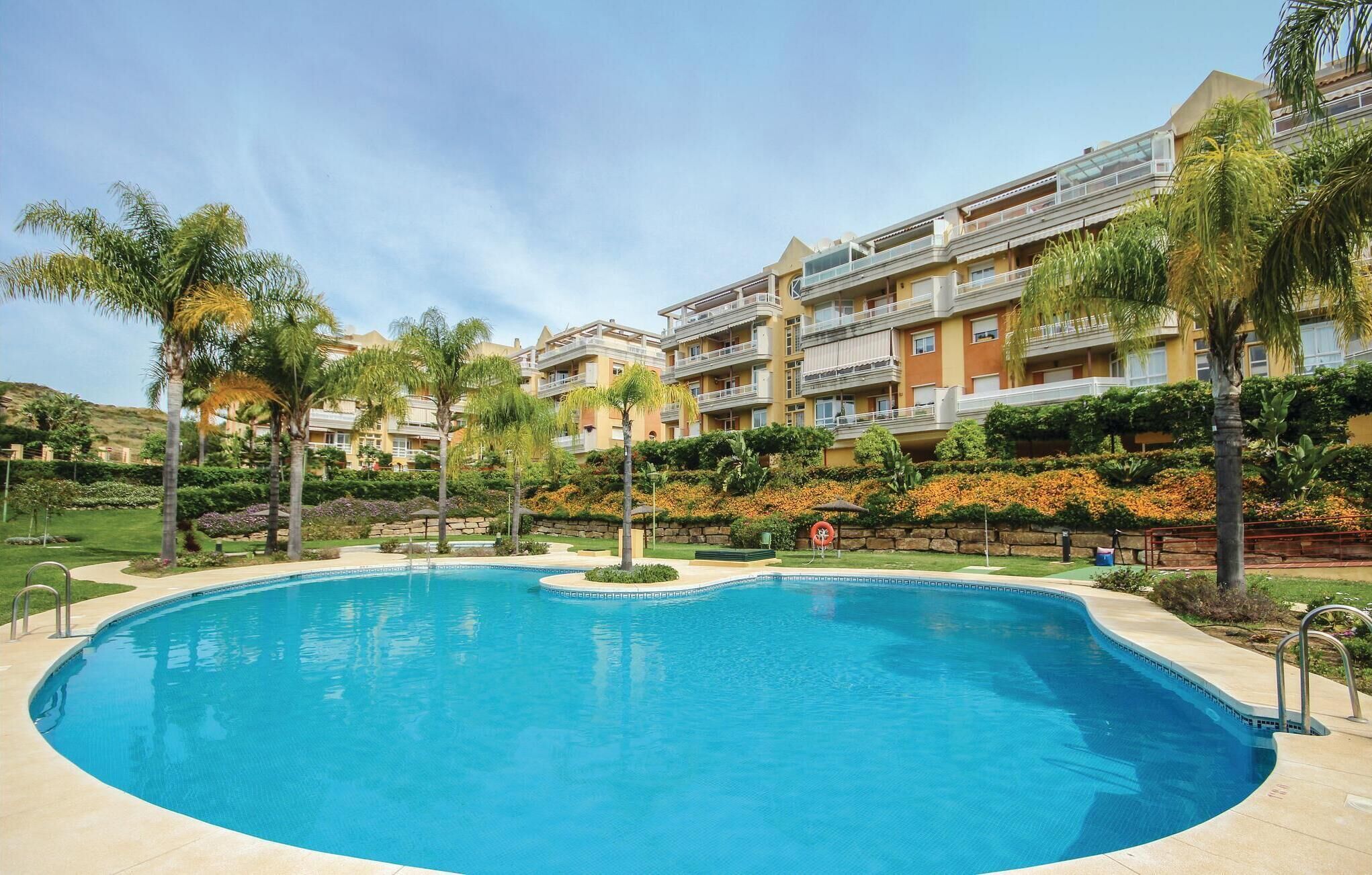 A swimming pool surrounded by palm trees and a multi-story building with balconies.