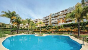 Una piscina rodeada de palmeras y un edificio de varios pisos con balcones.