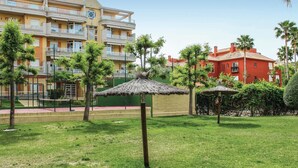 Un patio con un pabellón de techo de paja, una zona de piscina y un edificio de varios pisos con balcones.