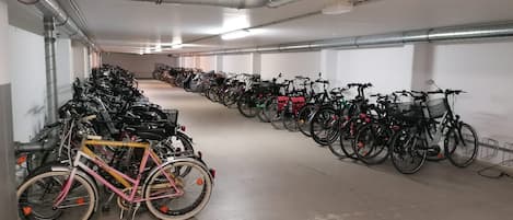 Un vaste espace de stationnement intérieur, vide, où s’alignent des rangées de vélos et de scooters.