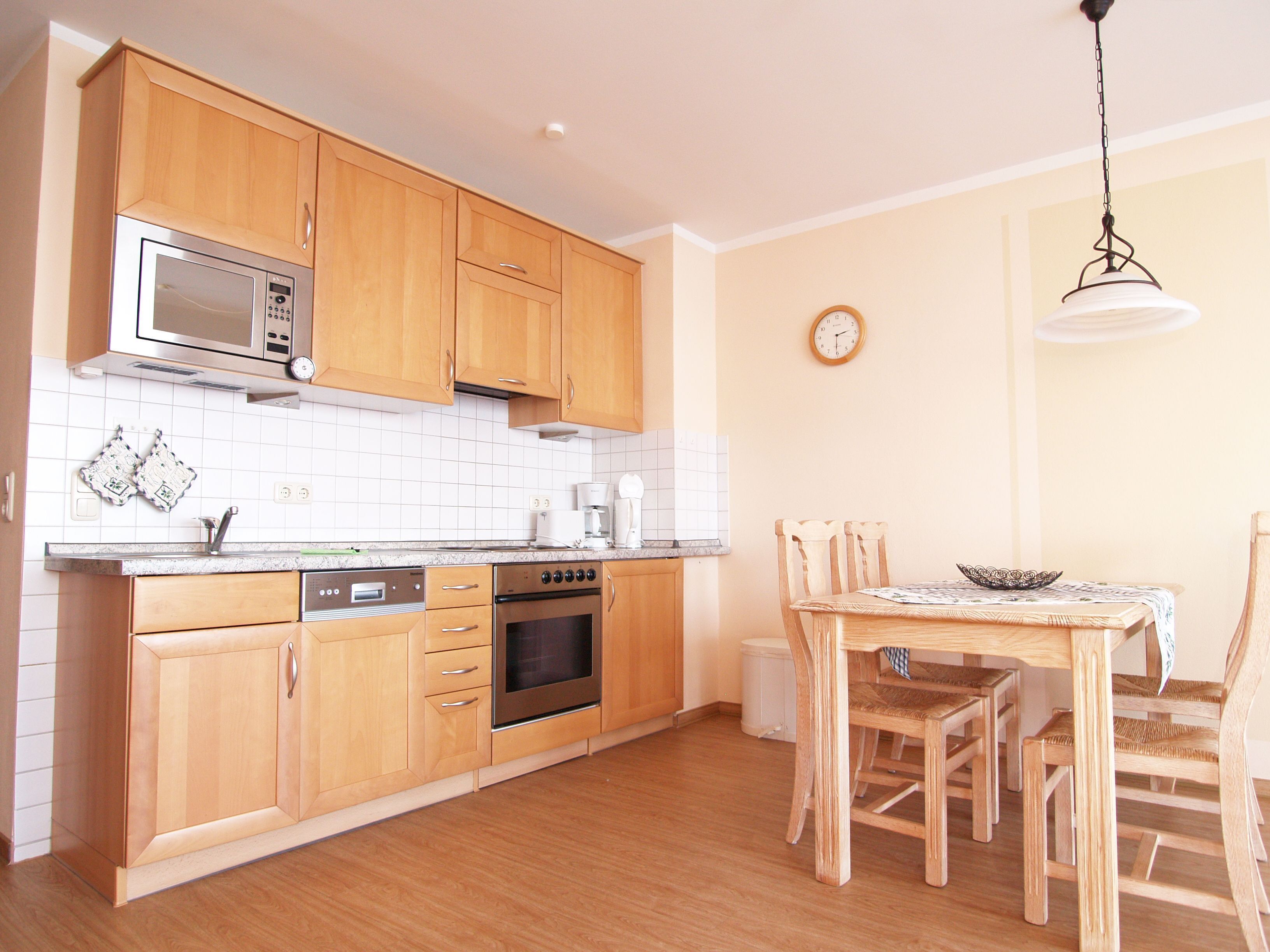 A kitchen with wooden cabinets, a microwave, an oven, a sink, and a dining table with chairs.
