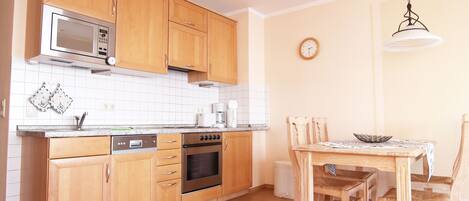 A kitchen with wooden cabinets, a microwave, an oven, a sink, and a dining table with chairs.