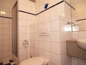 Ein Badezimmer mit weißen Fliesen, einer Toilette, einer Dusche und einem Waschbecken mit einer Granit-Arbeitsplatte.