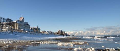 Un pueblo costero con edificios históricos, una playa cubierta de nieve y hielo, y un cielo despejado.