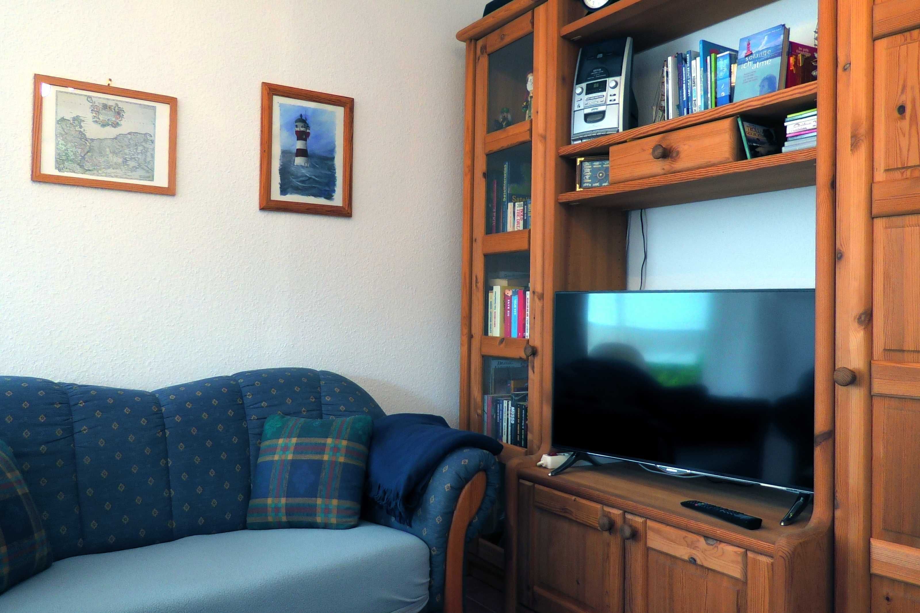 Una sala de estar con un sofá azul, un mueble de madera para centro de entretenimiento con un televisor de pantalla plana y dos cuadros enmarcados en la pared.