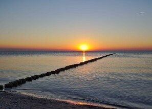 Een zonsondergang boven een rustige zee met een houten aanlegsteiger die zich in het water uitstrekt.