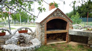 A stone-built outdoor fireplace with a brick chimney, surrounded by a stone wall and a grassy area. - Studio mit Klimaanlage und Balkon (Seline)