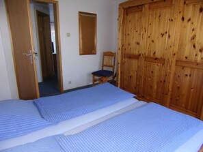 A bedroom with two beds, a wooden wardrobe, a chair, and a mirror on the wall.
