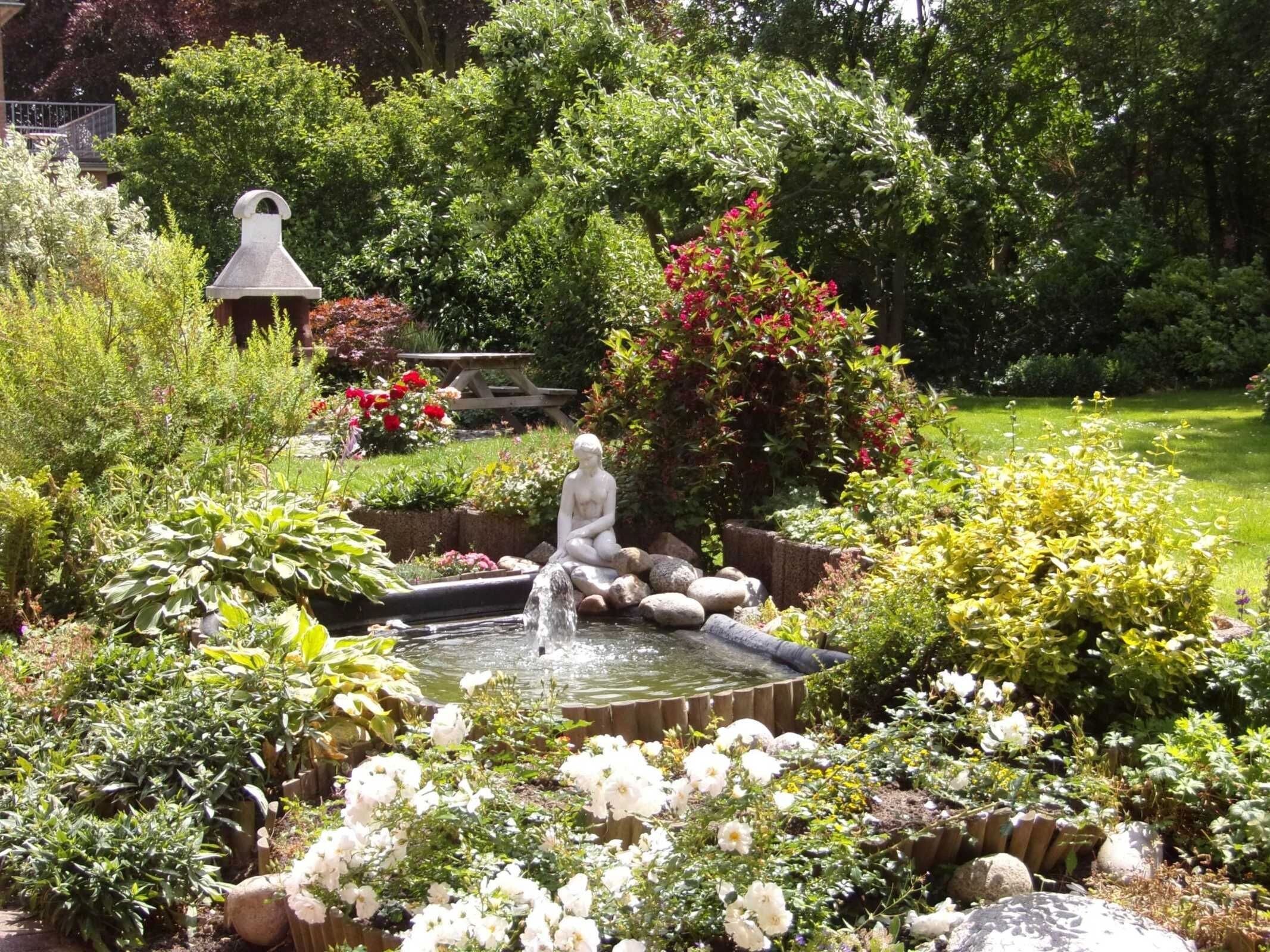 Un jardin agrémenté d’une fontaine, d’une statue et de diverses plantes.