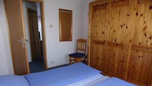 Une chambre avec deux lits, une armoire en bois, une chaise et un miroir au mur.
