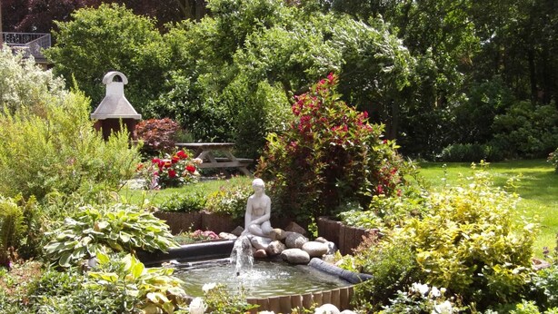 Un jardin agrémenté d’une fontaine, d’une statue et de diverses plantes.
