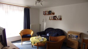 Un salon comprenant un canapé, deux fauteuils, une petite table avec des boissons et un téléviseur.