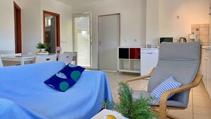 A modern hotel room with a bed, a seating area with a chair, a small table, and a kitchenette.