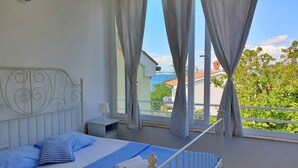 A bedroom with a bed, a nightstand, and a view of the sea.