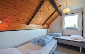 A room with two beds, wooden ceiling beams, a hanging light fixture, and a window with curtains.