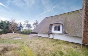 A traditional thatched-roof house with a small window, surrounded by a grassy area and trees.