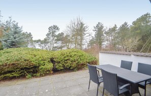 A patio with a table and chairs, surrounded by a hedge and trees.