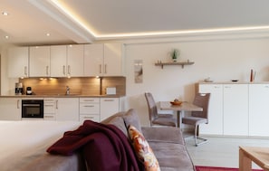 A modern hotel room with a kitchenette, a dining area, and a bed with a red blanket. - Cozy apartment in Binz with house sea view (Prora/Rügen)