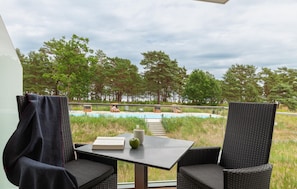 A balcony with wicker chairs and a table, overlooking a swimming pool and a forested area. - Cozy apartment in Binz with house sea view (Prora/Rügen)