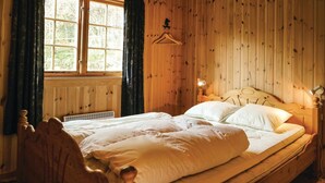 Una habitación de madera con una cama, una ventana y una lámpara fijada a la pared.