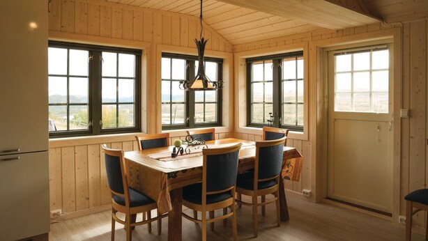 Comedor con paneles de madera, una mesa y sillas, ventanas amplias con vistas, y un colgador de luz.