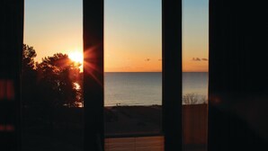 Vista pela janela com um pôr do sol sobre o mar, emoldurada pelas vidraças.