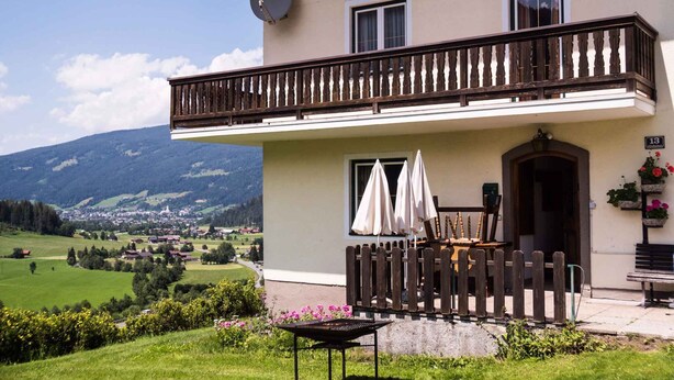 Ein zweistöckiges Gebäude mit einem Balkon, einer Satellitenschüssel und Blick auf eine gebirgige Landschaft.