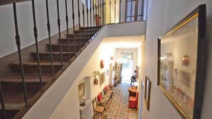 Uma escadaria leva a um corredor com piso estampado, um radiador e vários objetos fixados na parede.