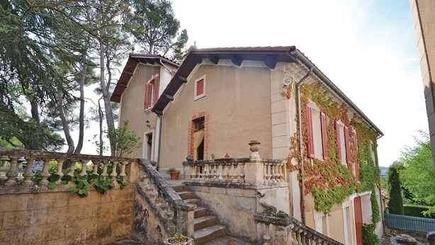 Edifício com escadaria de pedra que leva a uma varanda, rodeado de vegetação.