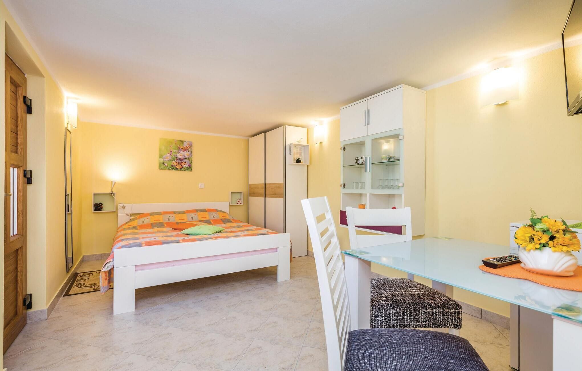 A bedroom with a bed, a desk, a chair, a wardrobe, and a small shelf with items.