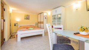 Een slaapkamer met een bed, een bureau, een stoel, een kledingkast en een klein plankje met spullen.