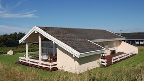 Uma casa pequena, térrea, com telhado inclinado, varanda coberta e um deck.