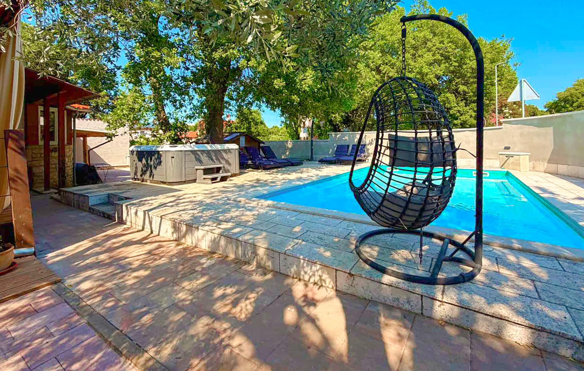A swimming pool with a hanging chair, lounge chairs, and a covered seating area.